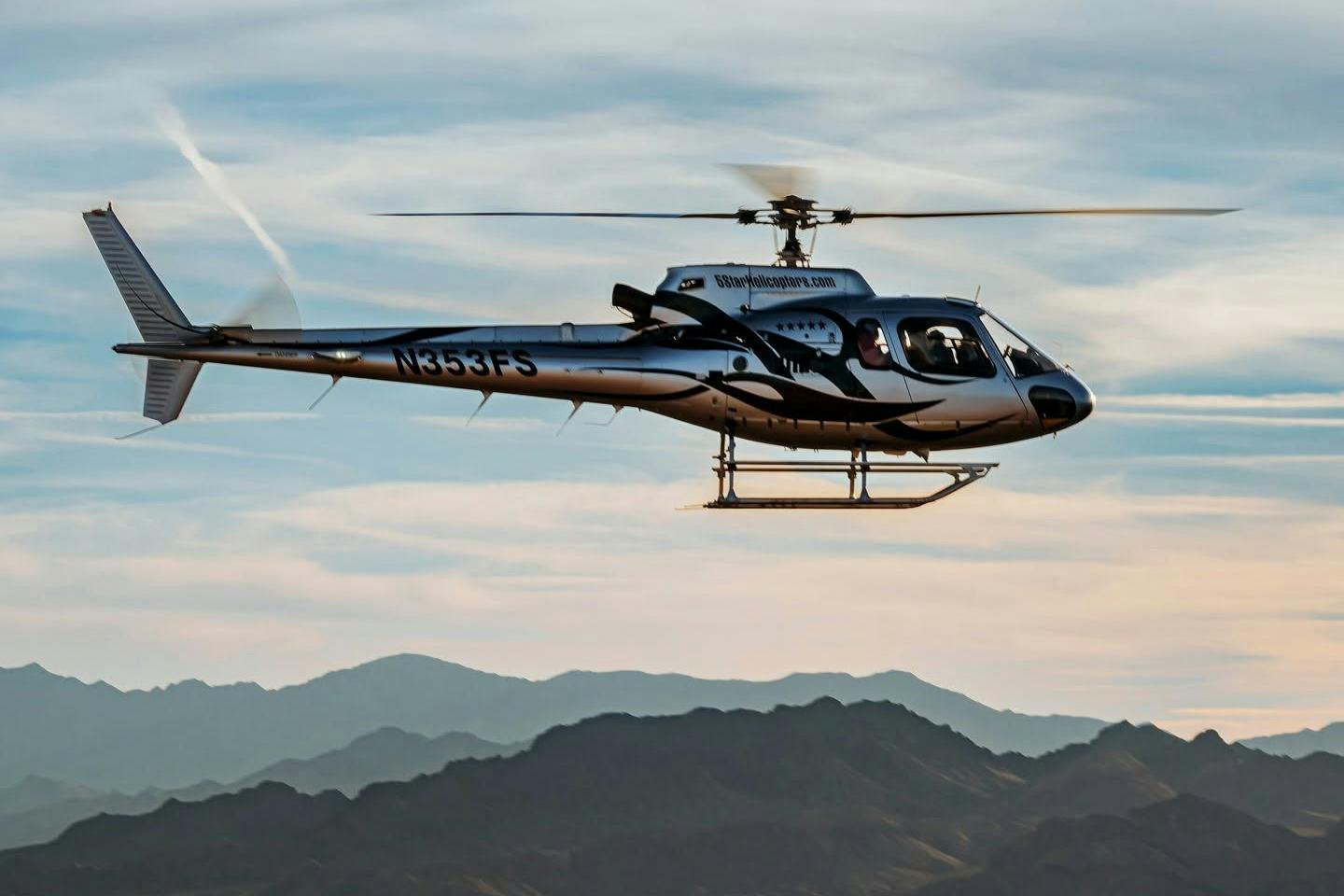 A helicopter in flight with mountains in the background under a partly cloudy sky.