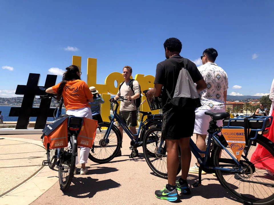 A group of people with bicycles gather around a large yellow sign on a sunny day, with clear blue skies in the background.