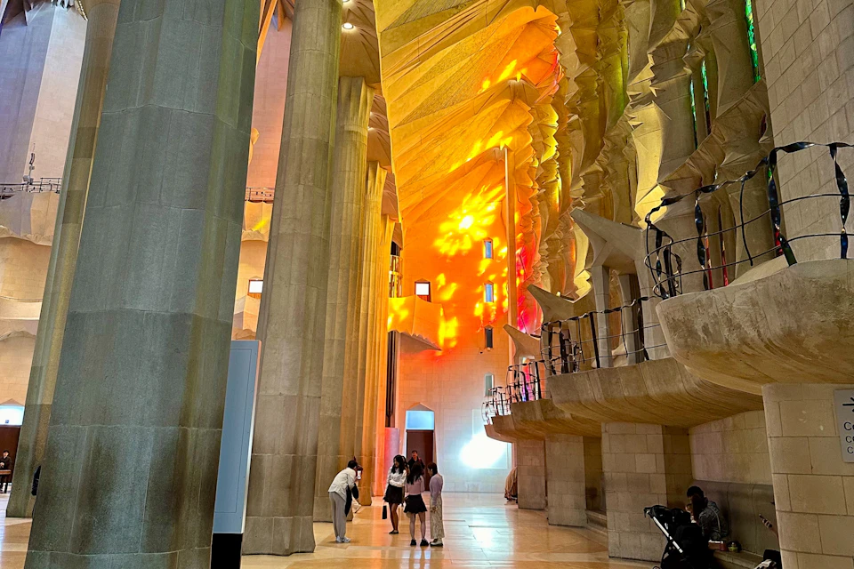 People inside a grand cathedral with colorful stained glass windows casting vibrant light patterns on the walls.