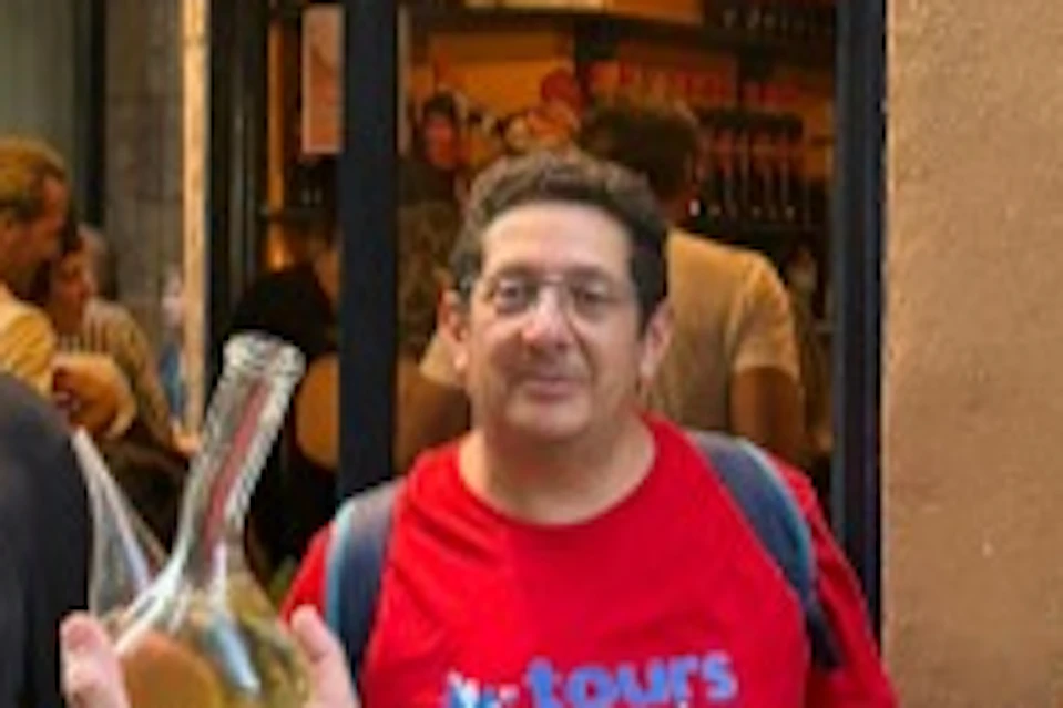 A group of people stand outside a shop, with one man holding a glass container of liquid. There are shelves and bottles visible inside.
