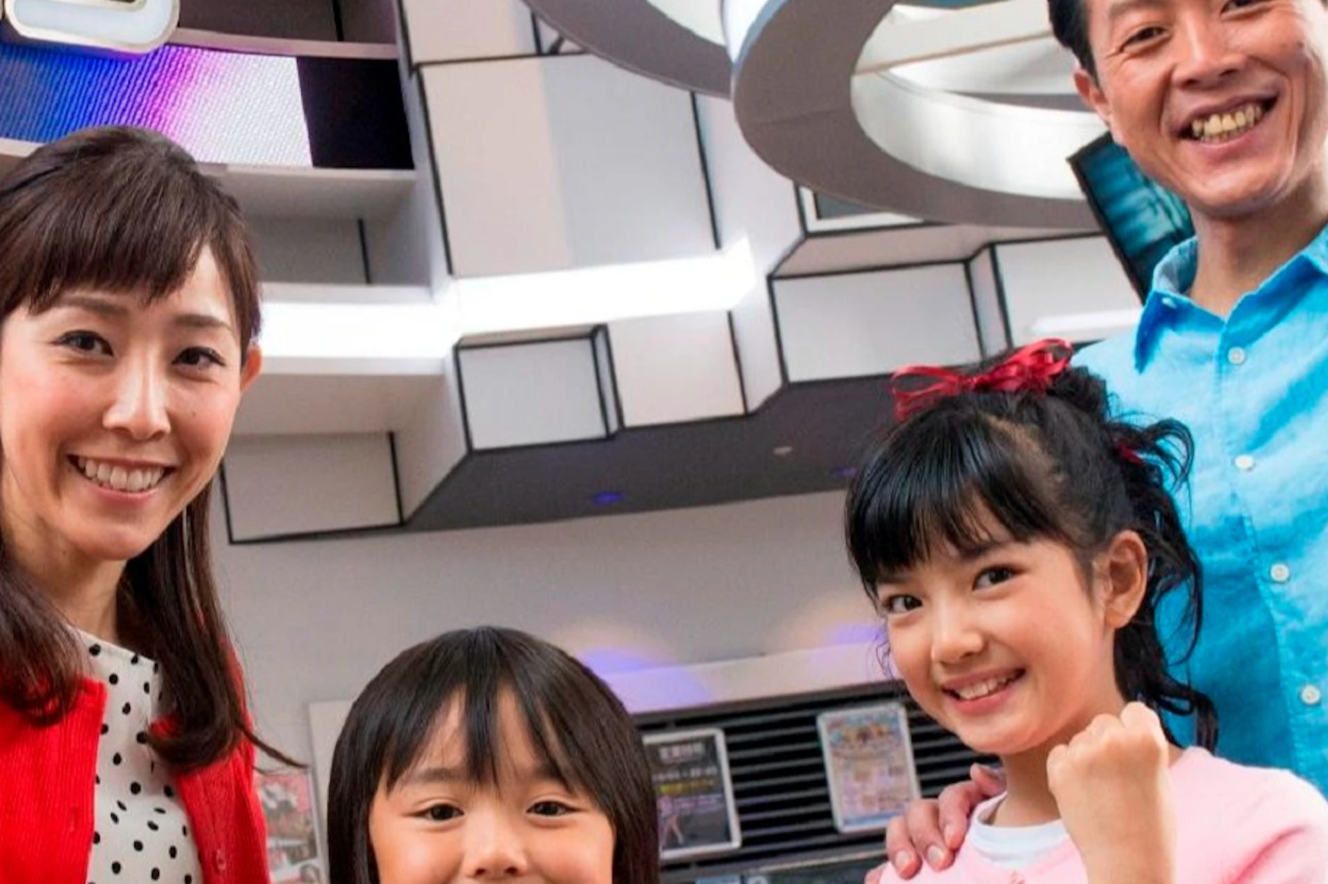 A smiling family of four poses with raised fists in front of a Sega Joypolis arcade entrance.