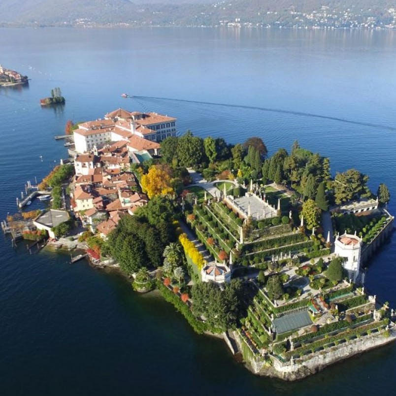 Vue aérienne d'une île avec des jardins, des bâtiments et une jetée, entourée d'un lac. Des collines sont visibles à l'arrière-plan.