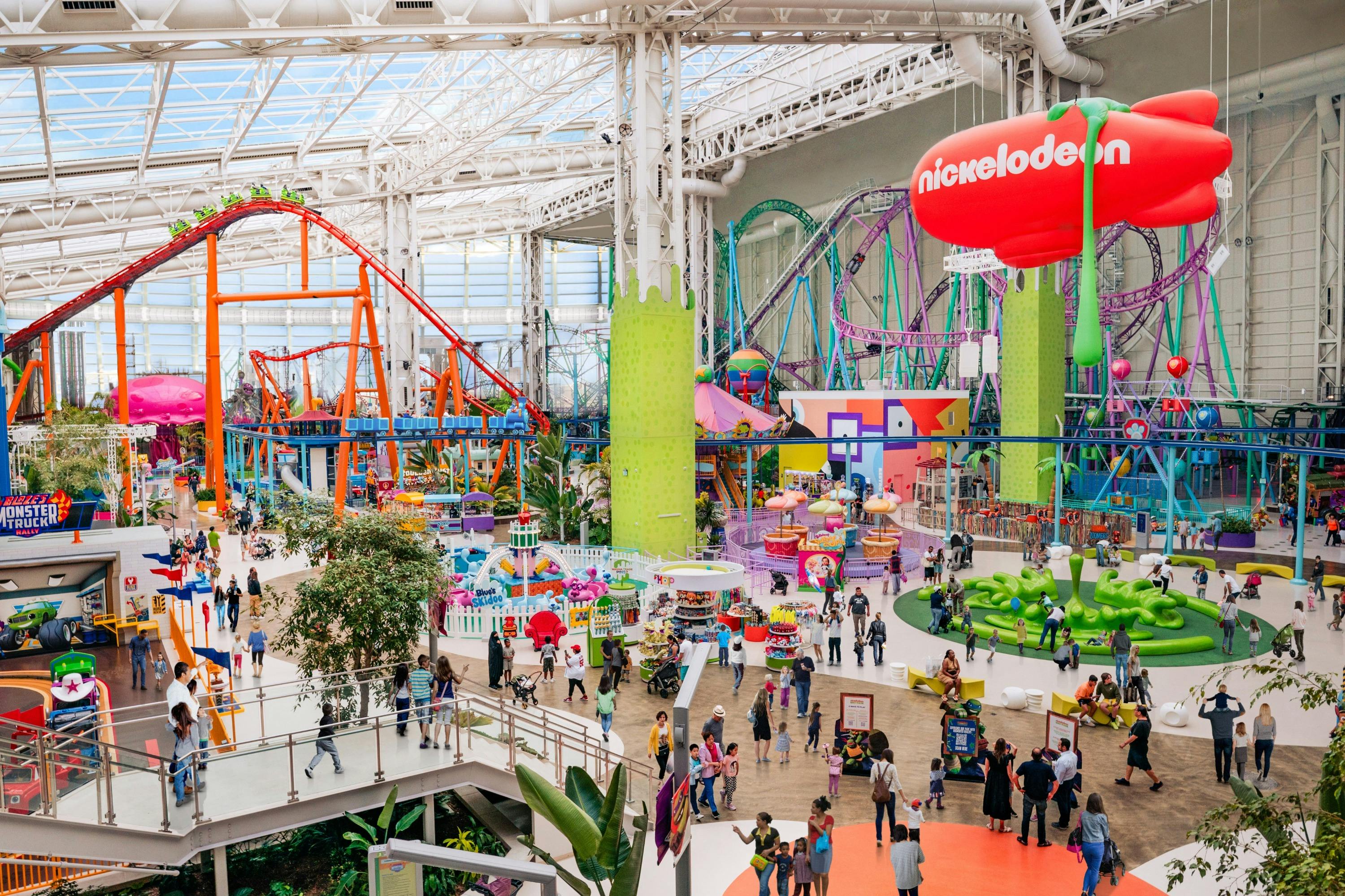 Indoor amusement park with colorful rides, roller coasters, and many people walking and enjoying the attractions.