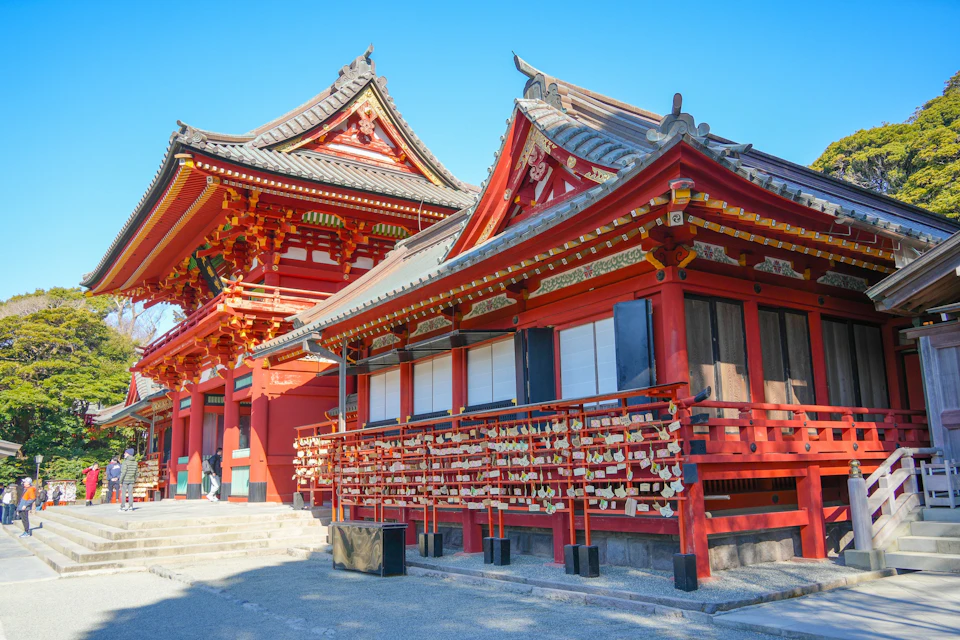 Traditional Japanese shrine buildings with red and gold accents, surrounded by clear blue sky and wooden ema plaques.