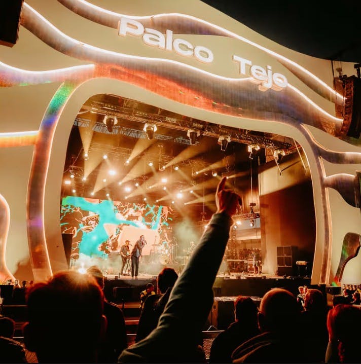 Una multitud gaudeix d'una actuació musical en directe en un escenari amb l'etiqueta "Palco Tejo", amb llums de colors i una pantalla al fons.