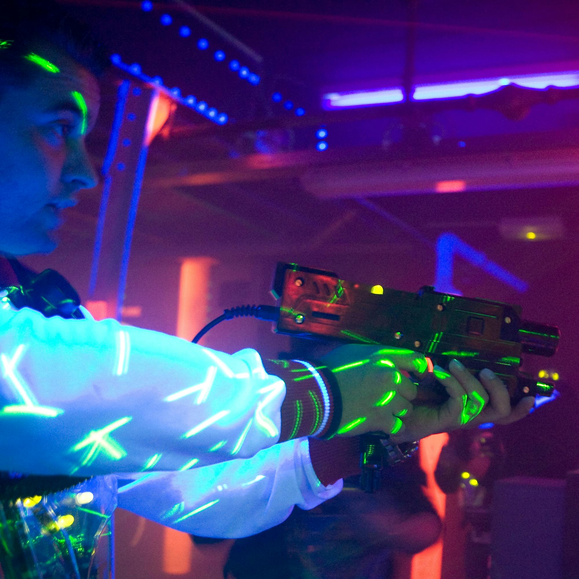 穿着白色夹克，设计明亮的人，在黑暗、霓虹灯照亮的环境中拿着激光标签枪。