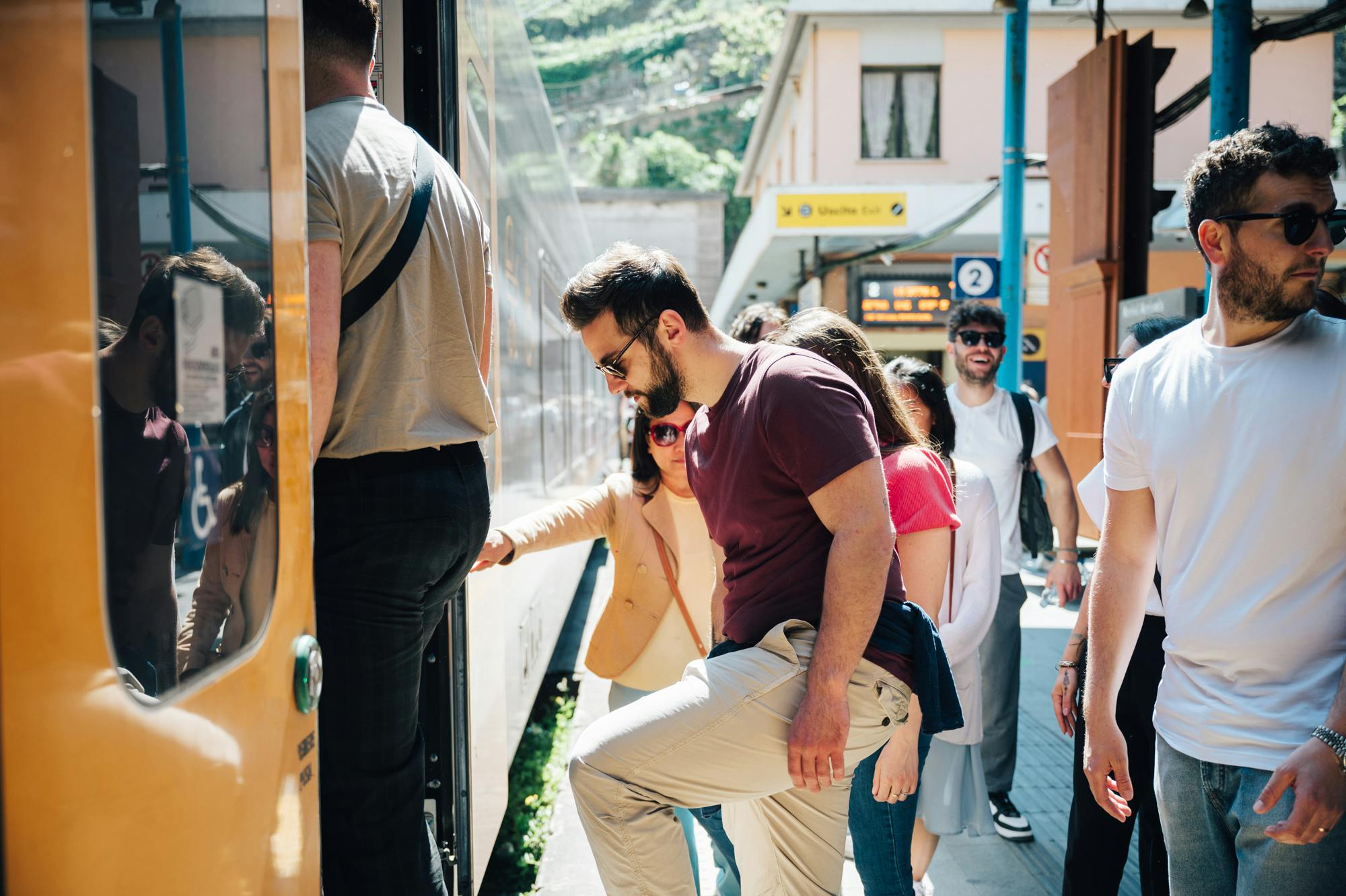 阳光明媚的日子，人们在车站登上火车。 一位身穿栗色衬衫的男士和另一位身穿白色衬衫的男士显眼可见。