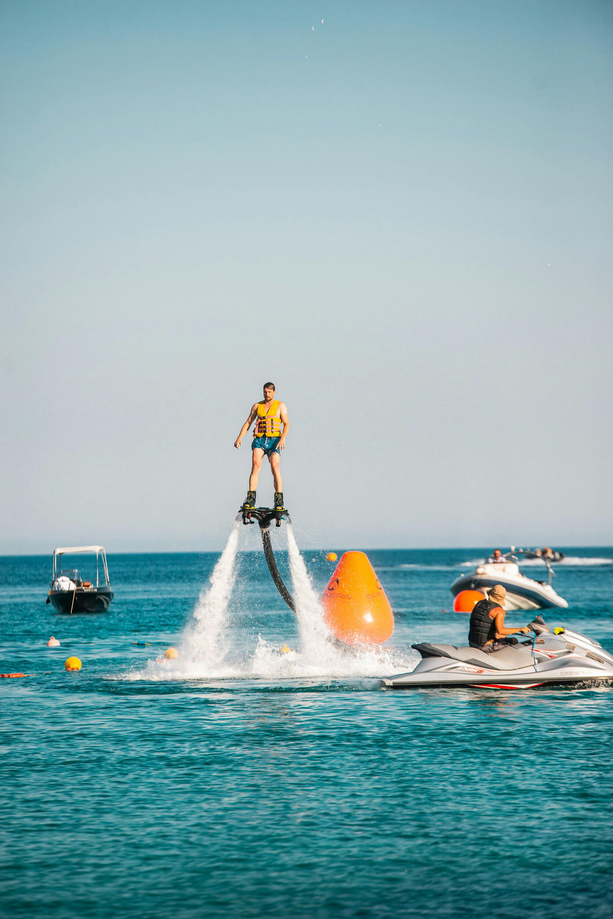 구명조끼를 입은 사람이 화창한 날 보트와 제트스키를 배경으로 물 위를 날고 있습니다.