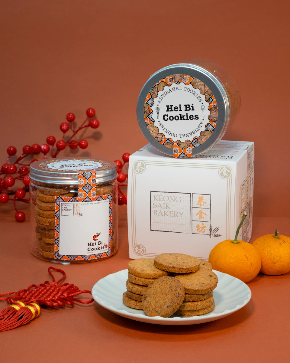 A display of Hei Bi Cookies in a jar, a box, and a plate, with oranges, red decorations, and a branch with red berries.