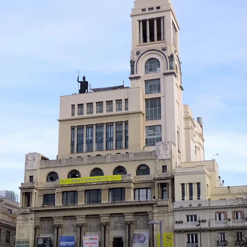 Hög, utsmyckad byggnad med en staty ovanpå, olika välvda fönster och banderoller som annonserar en konstskola och utställningar.