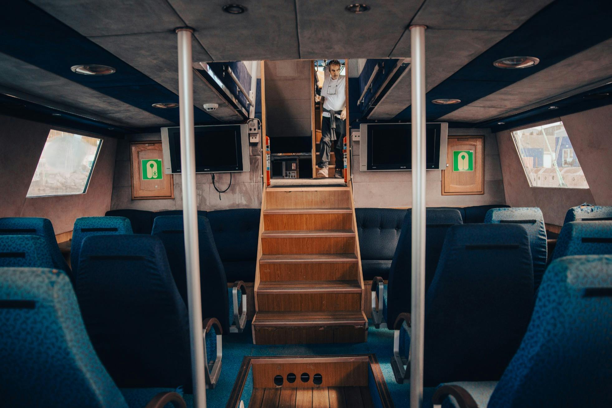 Interno di un veicolo o di un'imbarcazione con sedili blu, una scala di legno e una persona in piedi in cima alla scala.