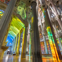 Interiör av en stor katedral med höga pelare, glasmålningar som gjuter färgglada ljusmönster på väggarna och golvet.