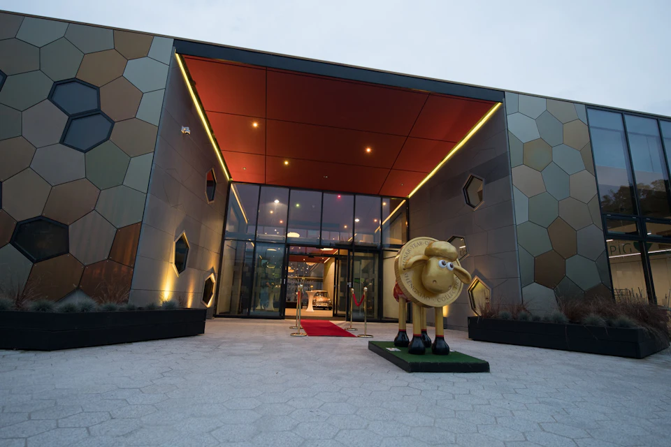 Entrance of a modern building with hexagonal exterior panels, red carpet, and a decorative sheep sculpture on a pedestal.