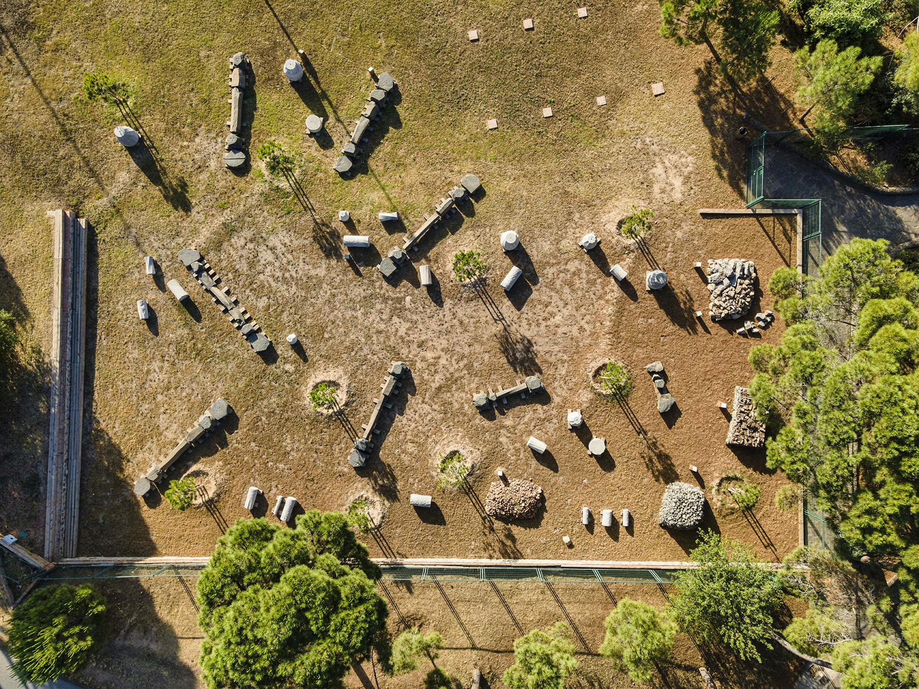 A bird's-eye view of an outdoor obstacle course with various logs, rocks, and trees on a dirt and grass field.
