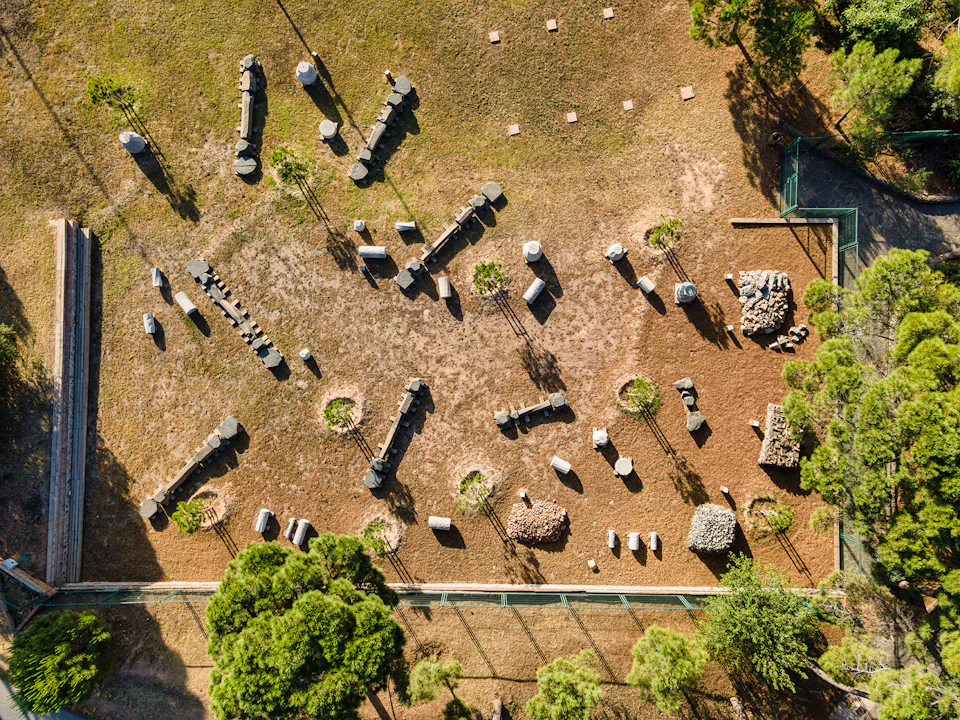 A bird's-eye view of an outdoor obstacle course with various logs, rocks, and trees on a dirt and grass field.