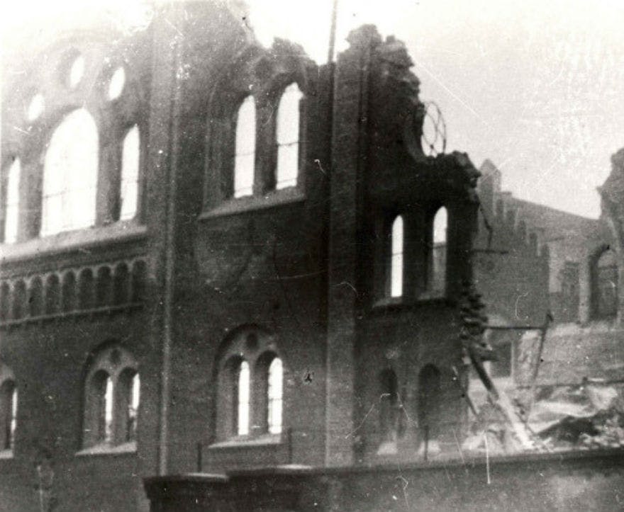 Κατεστραμμένο κτίριο από τούβλα με τοξωτά παράθυρα, μερική κατάρρευση και μπάζα. Η σκηνή φαίνεται παλιά και μονόχρωμη.