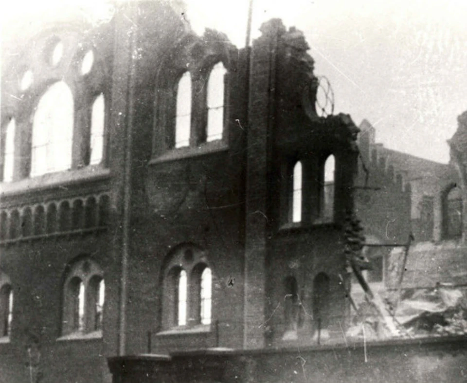 Damaged brick building with arched windows, partial collapse, and rubble. Scene appears old and monochrome.