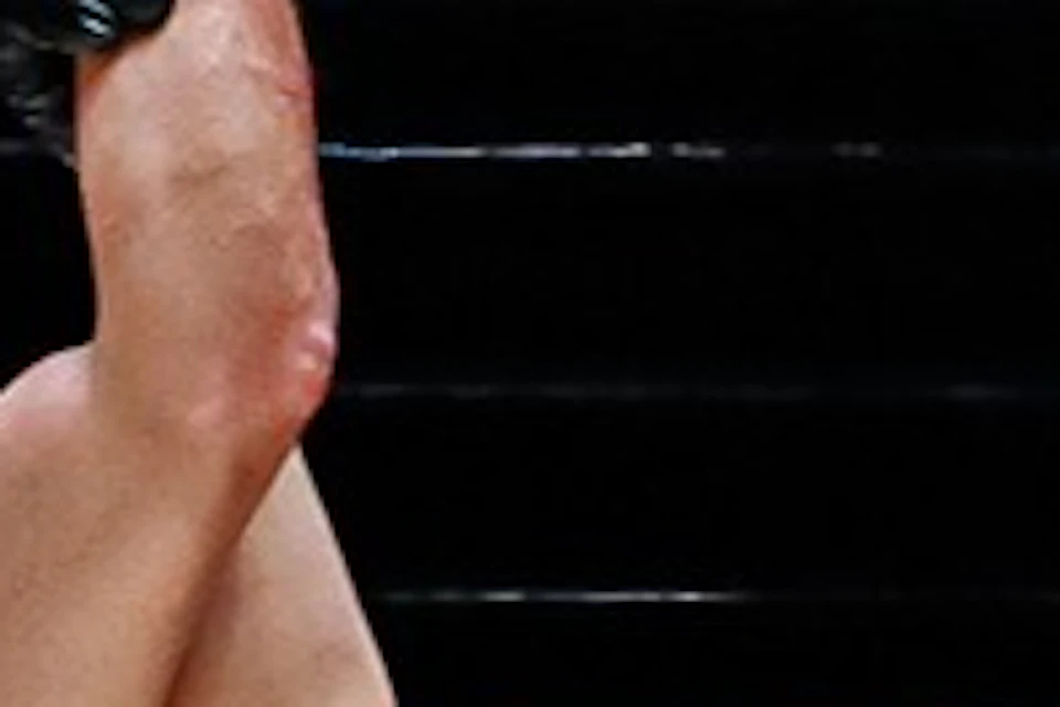Two Muay Thai fighters and a referee in a ring. Referee raises the hand of the winning fighter on the left.