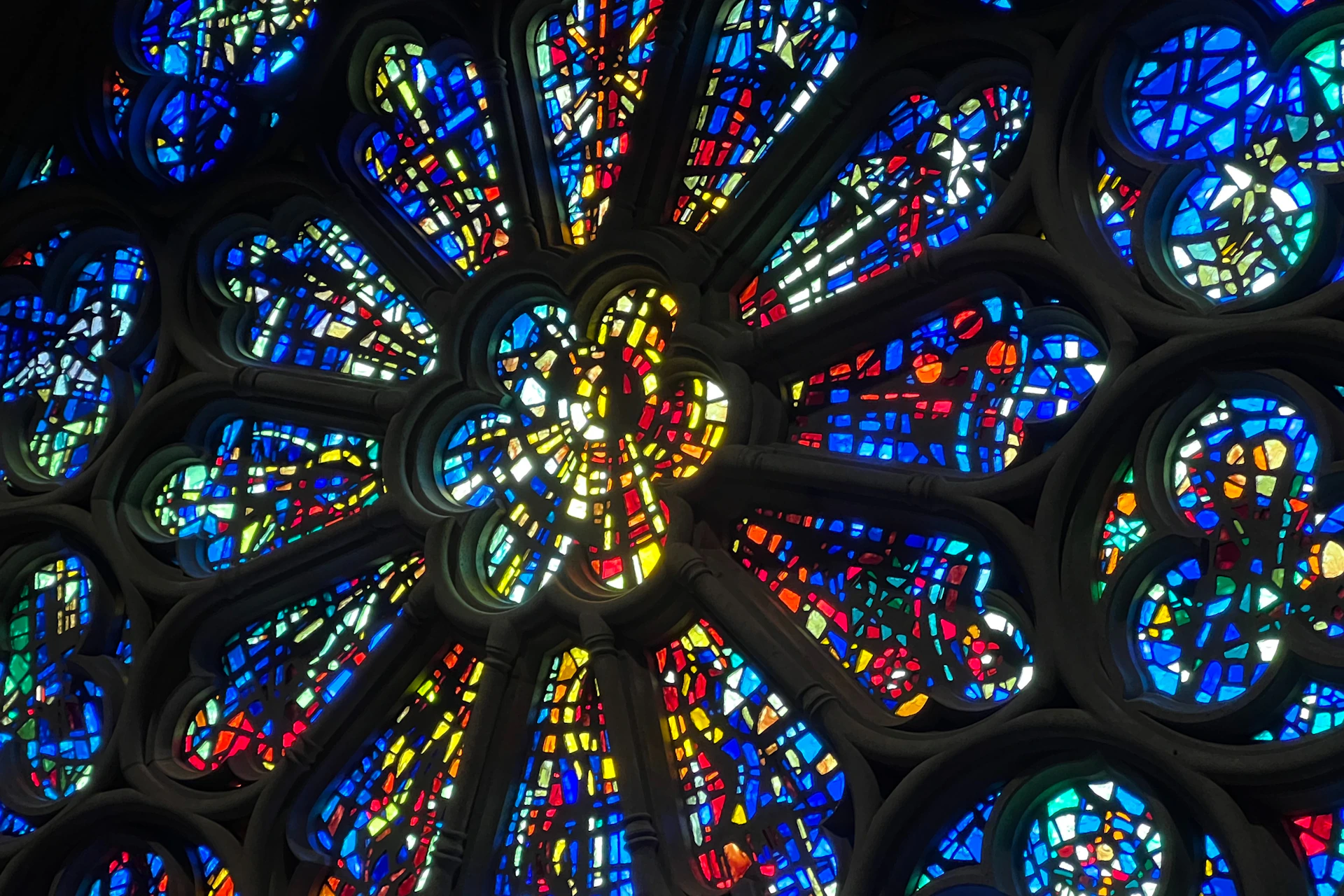 A close-up view of a stained glass rose window with colorful, symmetrical patterns illuminated by light.