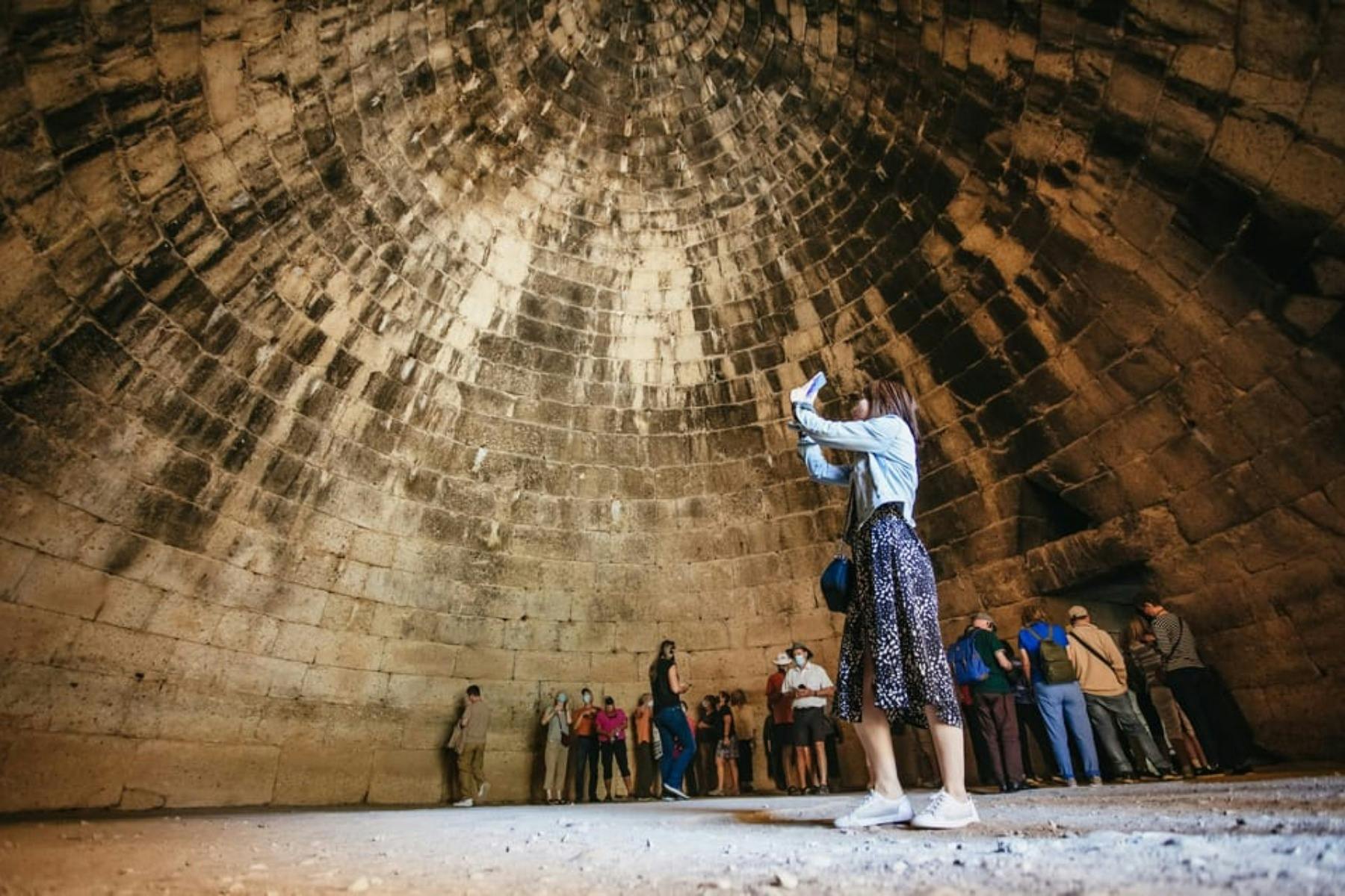 Tourists admire the high beehive-shaped stone dome of the Treasury of Atreus in Mycenae.