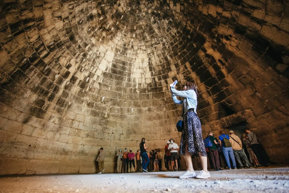 Tourists admire the high beehive-shaped stone dome of the Treasury of Atreus in Mycenae.