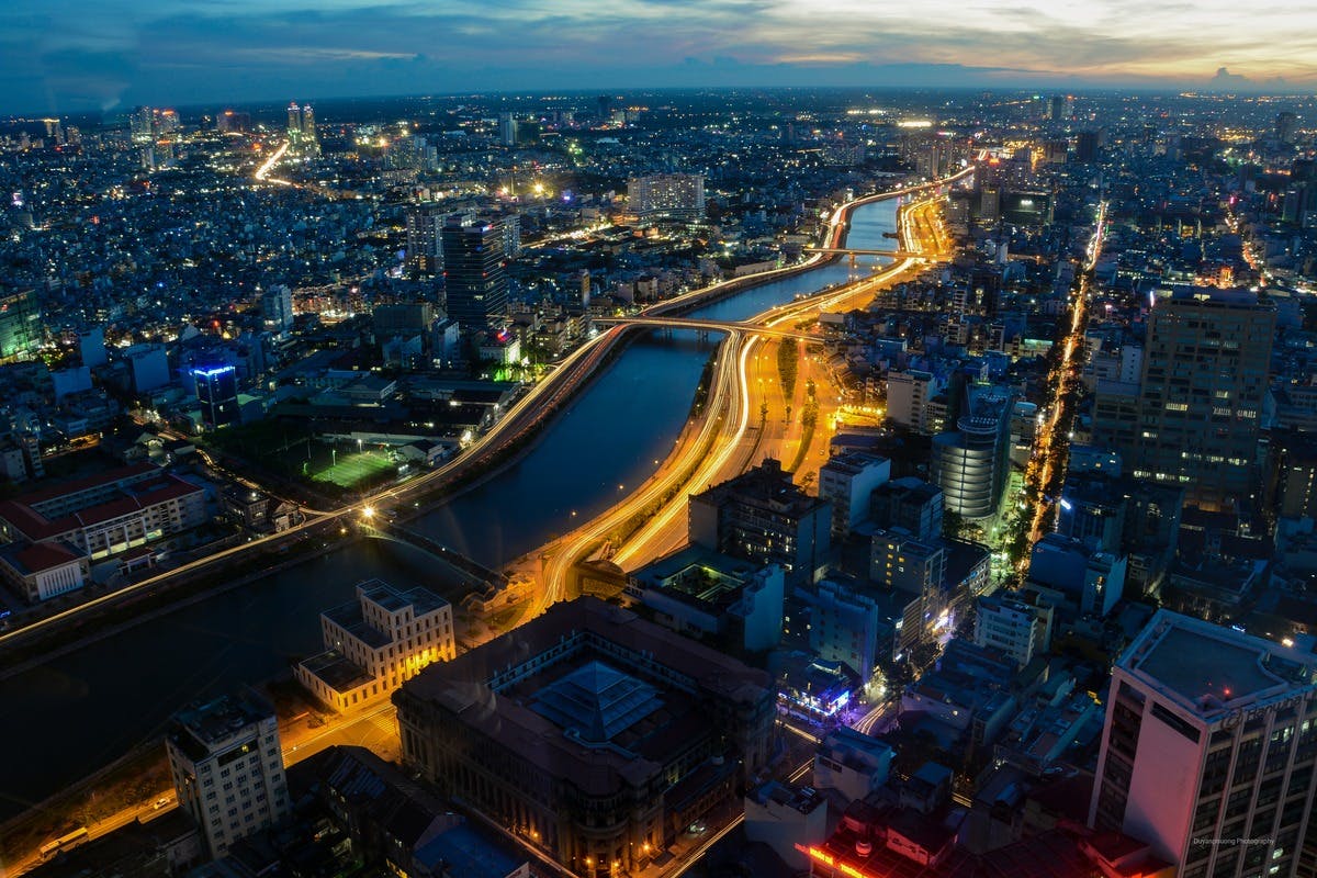 Aerial night view of a city with illuminated streets, a river running through it, and buildings densely packed on either side.