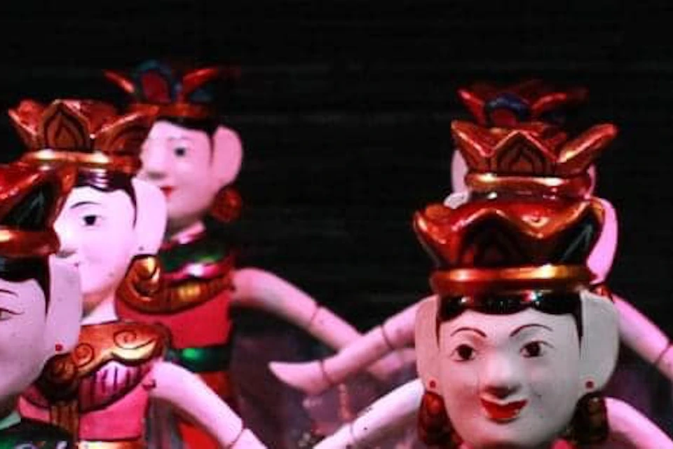 Traditional water puppets in colorful costumes performing on a water stage, illuminated in a dark setting.