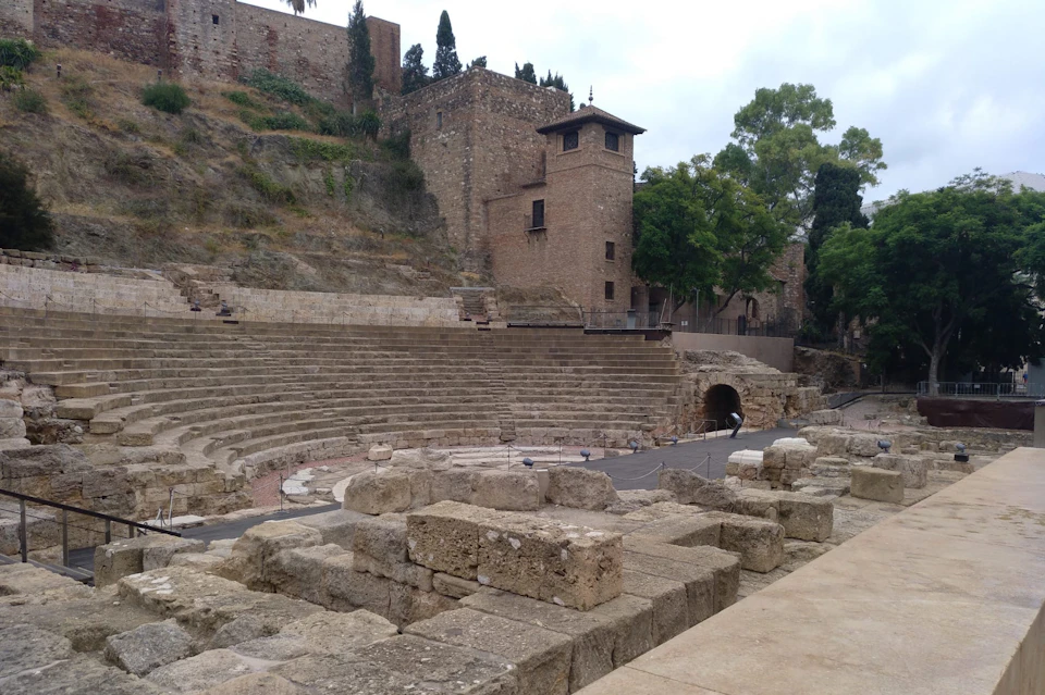 Ancient stone amphitheater with tiered seating, surrounded by rustic stone buildings and greenery.