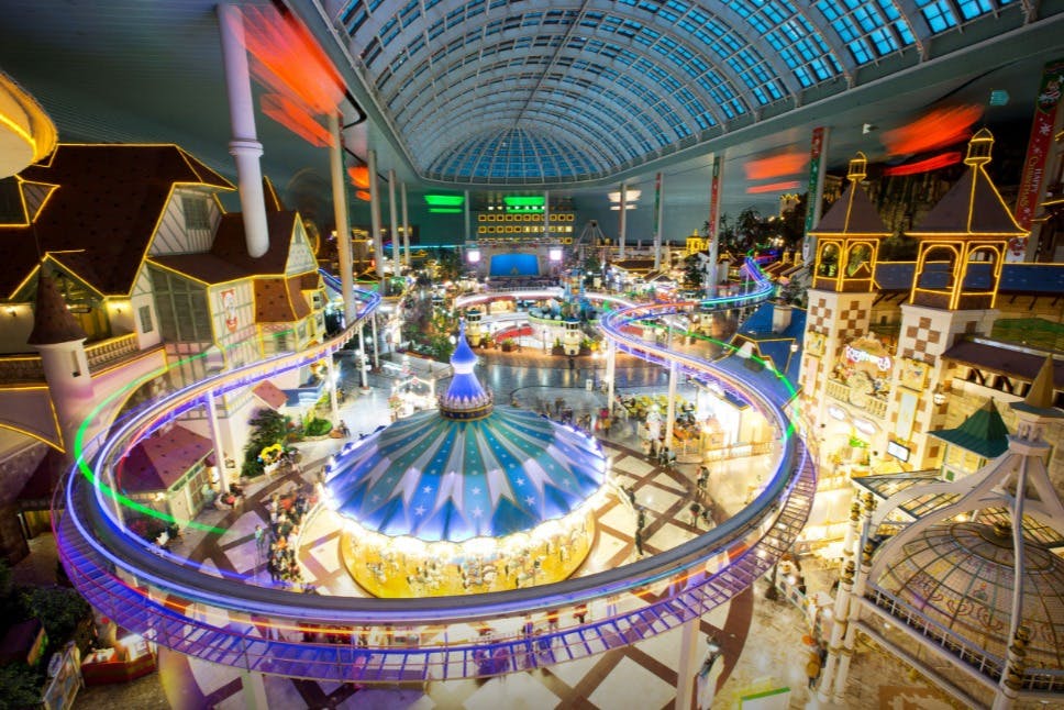 カルーセル、ジェットコースター、カラフルなライト、ガラスのドームの天井を備えた大きな屋内遊園地。