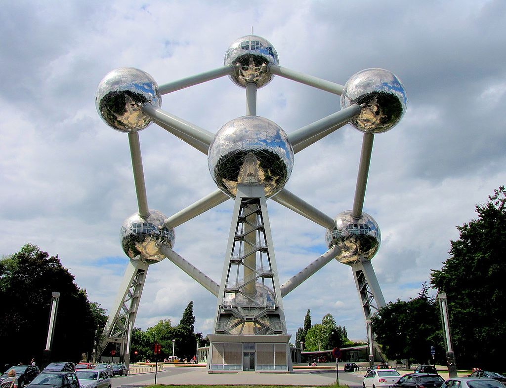 Una gran estructura compuesta de esferas y tubos metálicos interconectados, con coches y árboles rodeándola bajo un cielo nublado.