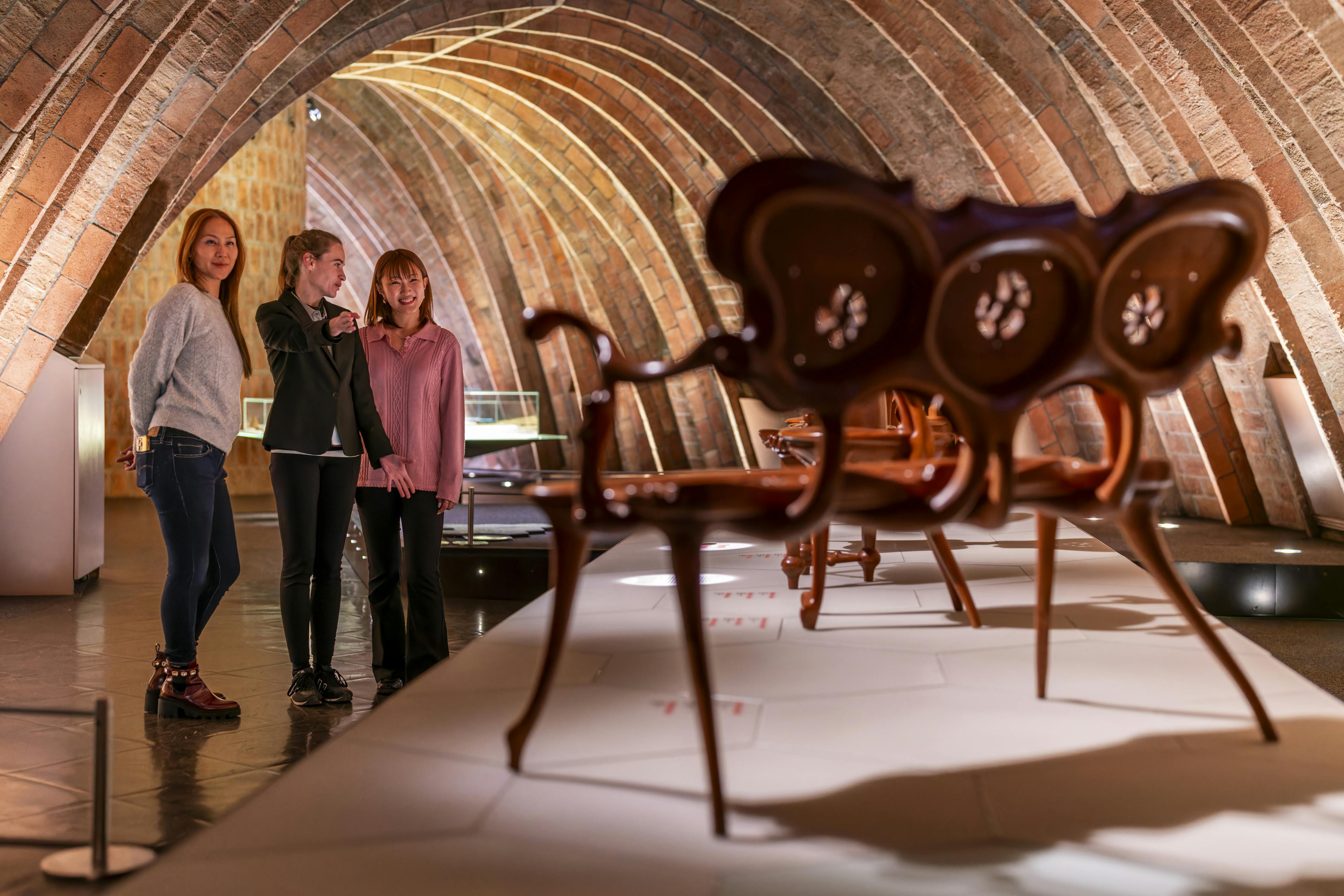 Tre donne che ammirano gli oggetti esposti in una stanza ad arco illuminata da una luce calda e con pezzi di arredamento esposti.