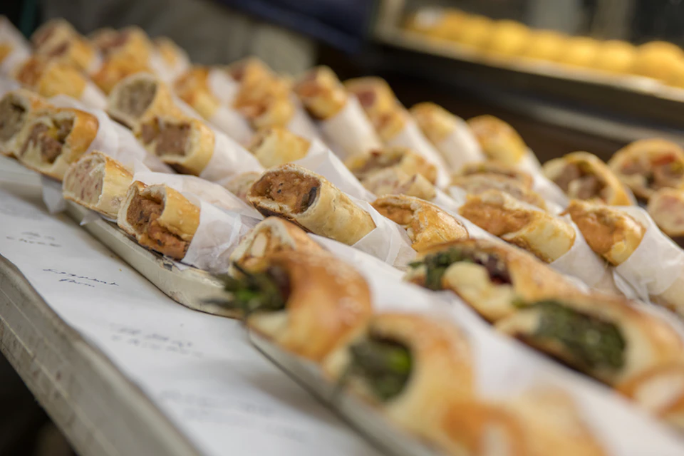 Rows of various filled pastries wrapped in paper, displayed on trays.