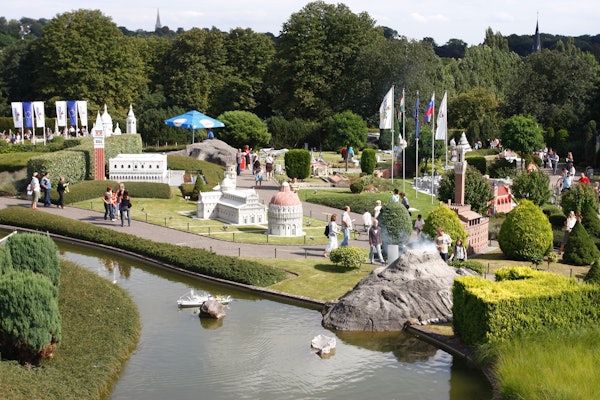 Gent passejant per maquetes en miniatura de llocs famosos en un parc amb vegetació i una petita via fluvial.