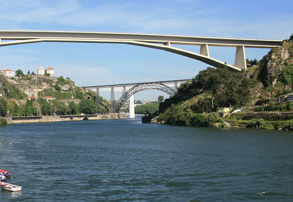 Two bridges span a river flanked by green hills and cliffside buildings under a clear blue sky.