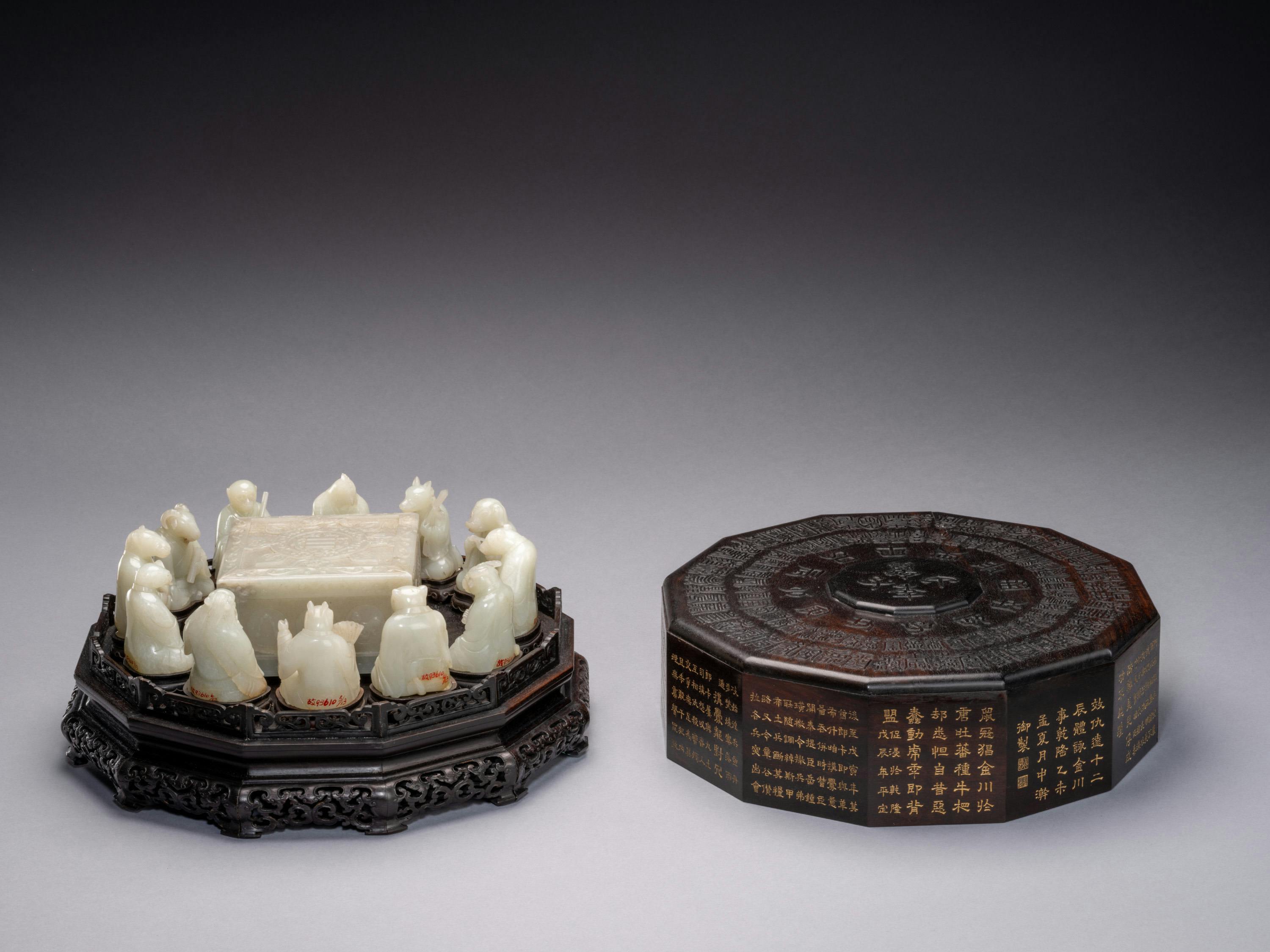 A carved sculpture set with a black base featuring jade figurines arranged around a central piece, next to an ornate black cover.