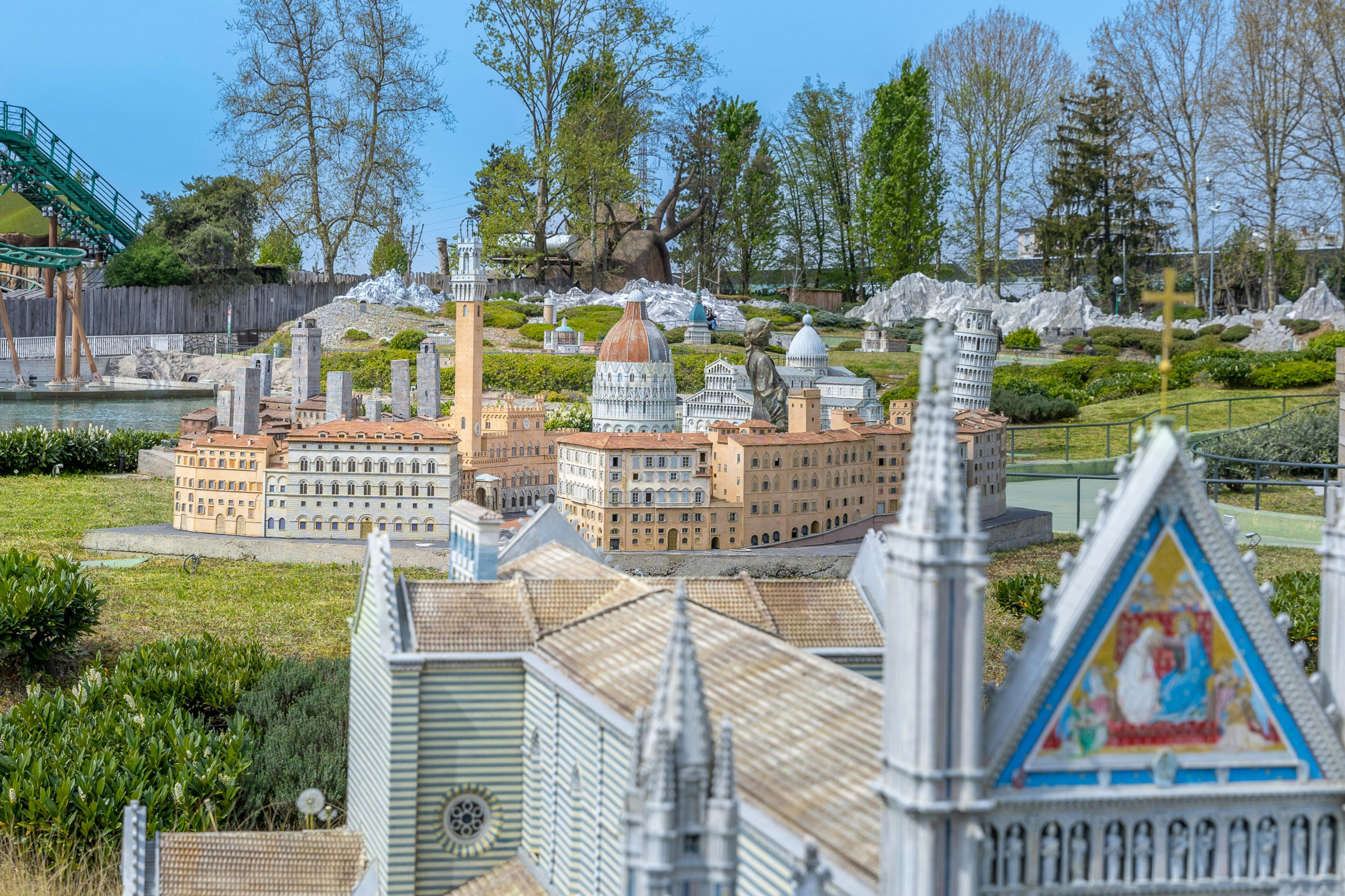 A miniature model of Italian landmarks, including domed buildings and towers, displayed outdoors with trees in the background.