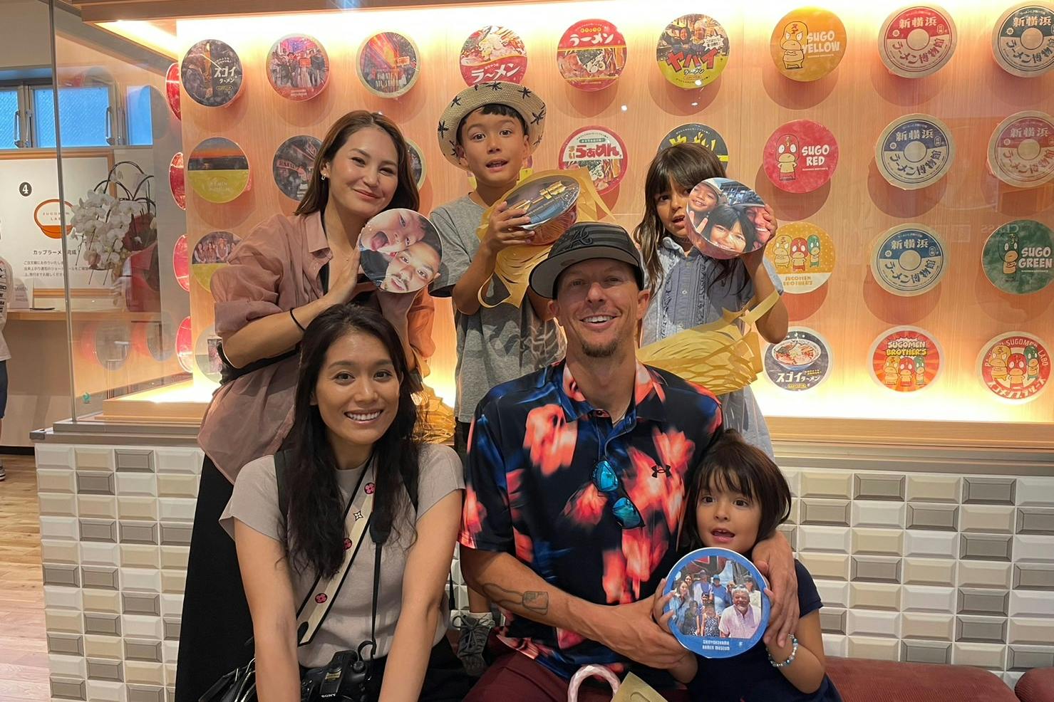 A group of people posing together indoors, holding circular items with images on them, in front of a decorated wall.