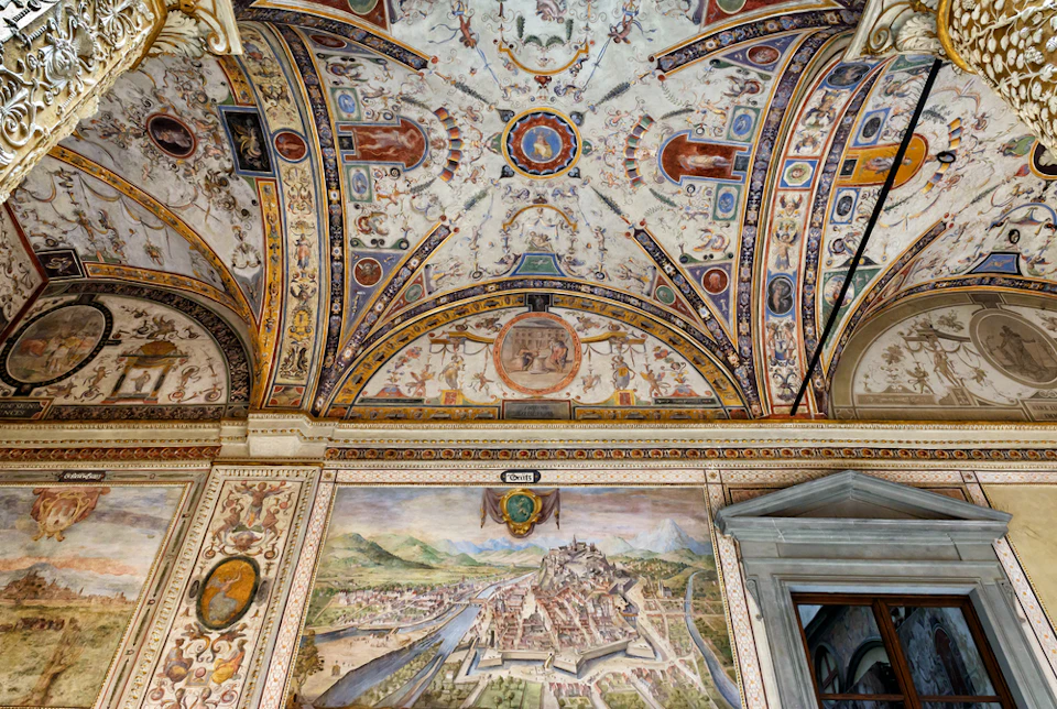Ornate ceiling fresco and detailed wall mural depicting a historical townscape with a river and mountains.