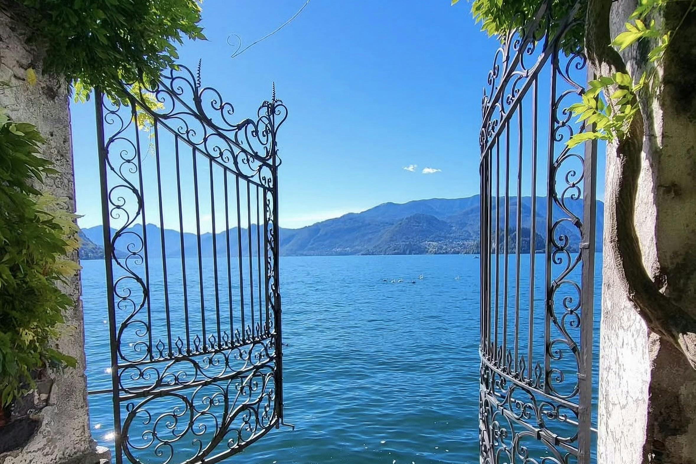 Ornate iron gates open to a scenic view of a calm lake surrounded by distant hills under a clear blue sky.