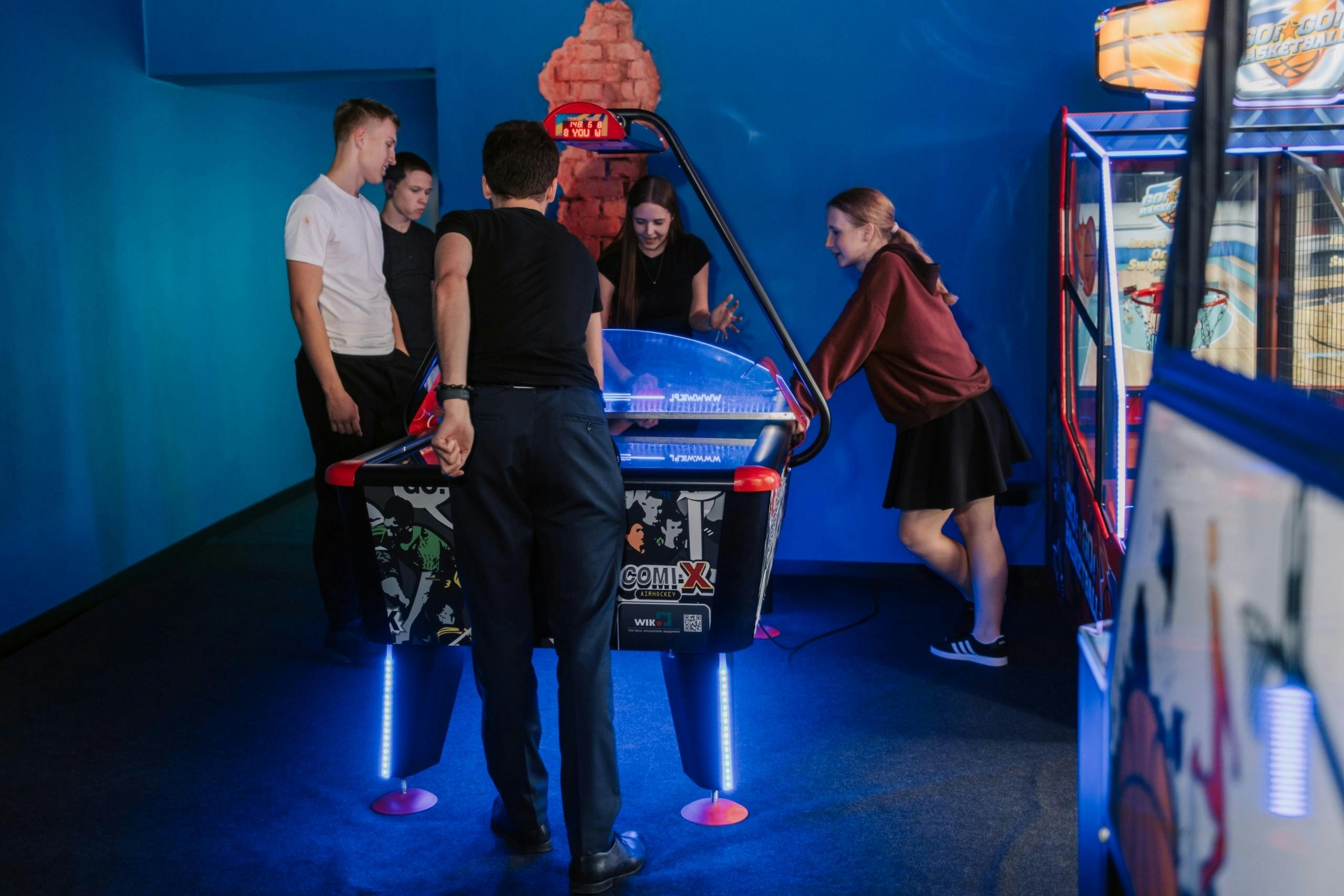 A group of four people around an air hockey table in a room with blue walls and a red decorative brick feature.