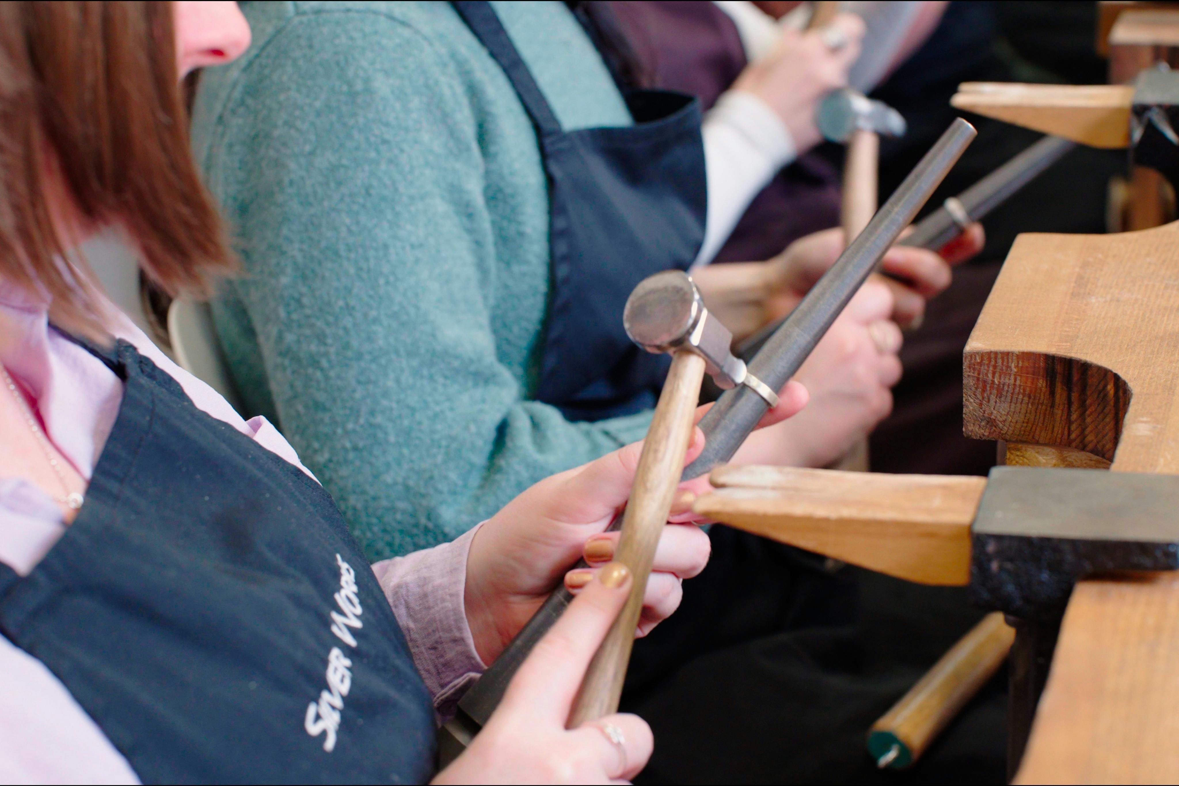 Close-up of people holding hammers and metal rods while wearing aprons during a hands-on workshop.