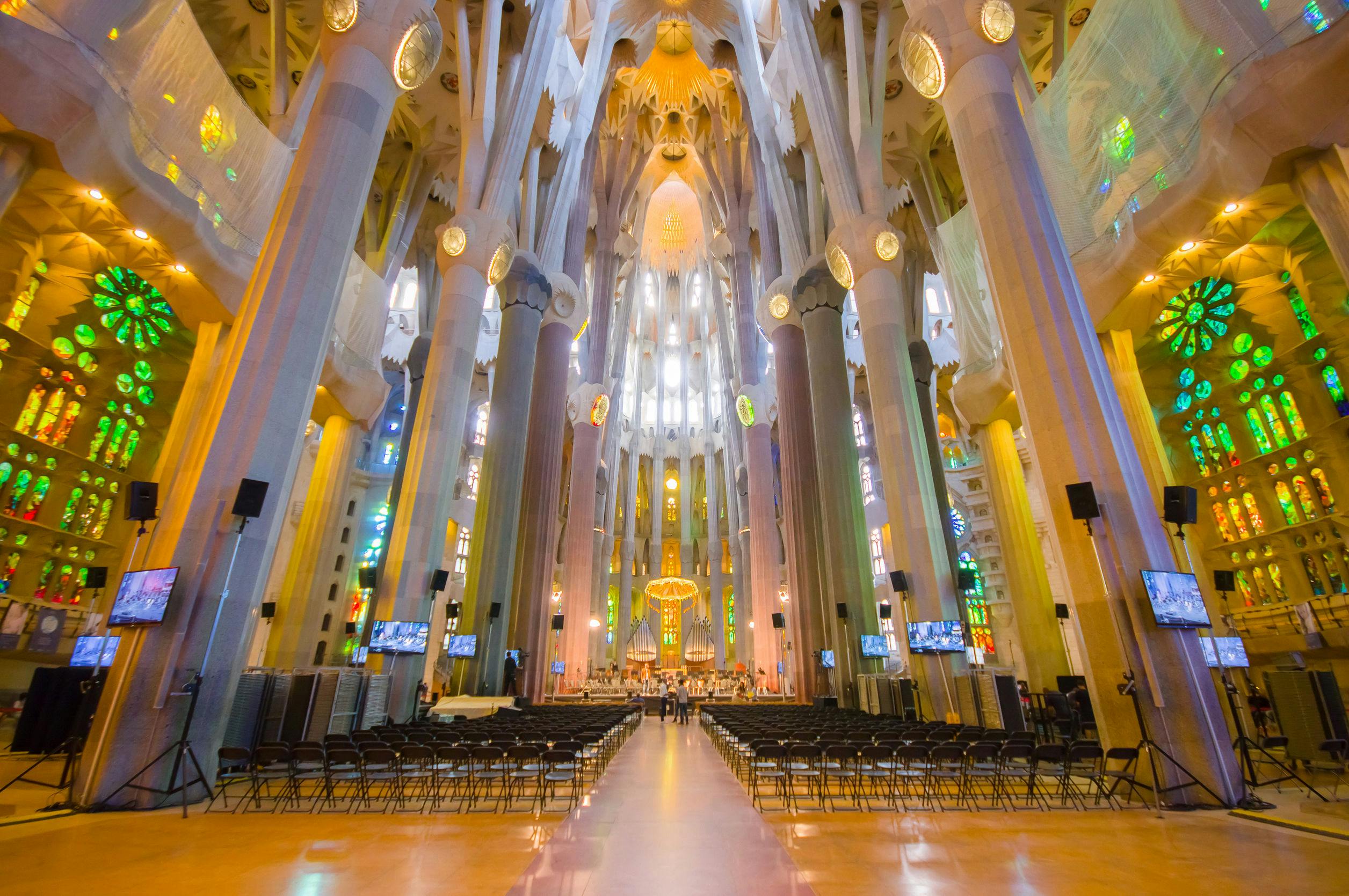 Interior of a large cathedral with tall columns, stained glass windows, and rows of empty chairs facing an ornate altar.