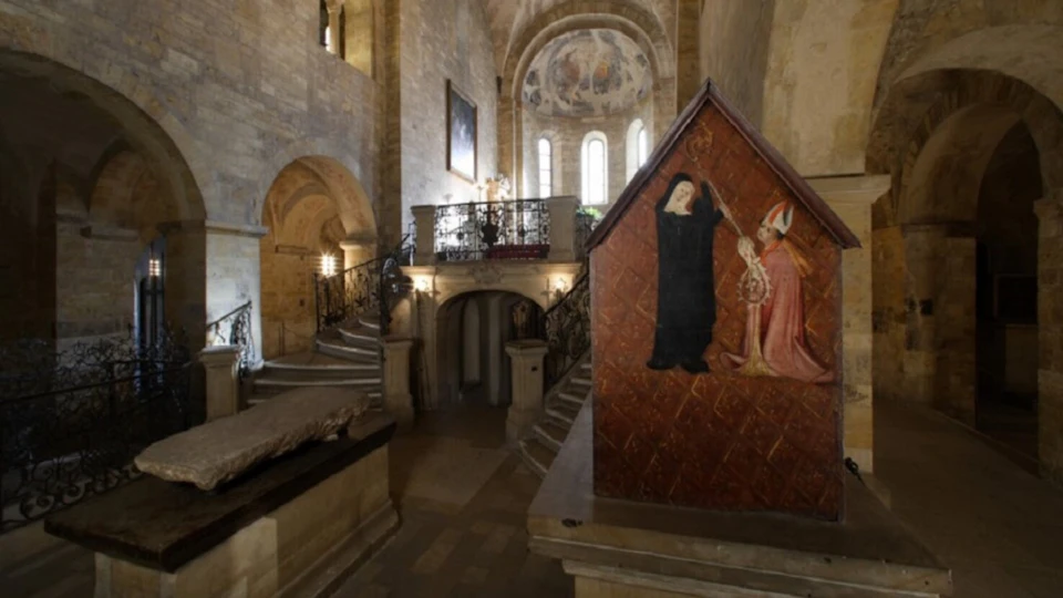 Ornate interior of an ancient church with stone walls, arched doorways, a staircase, and a painting of religious figures.