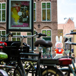 Cyklar parkerade framför en byggnad med grönklädda fönster, med en stor tecknad kaninstaty i bakgrunden.