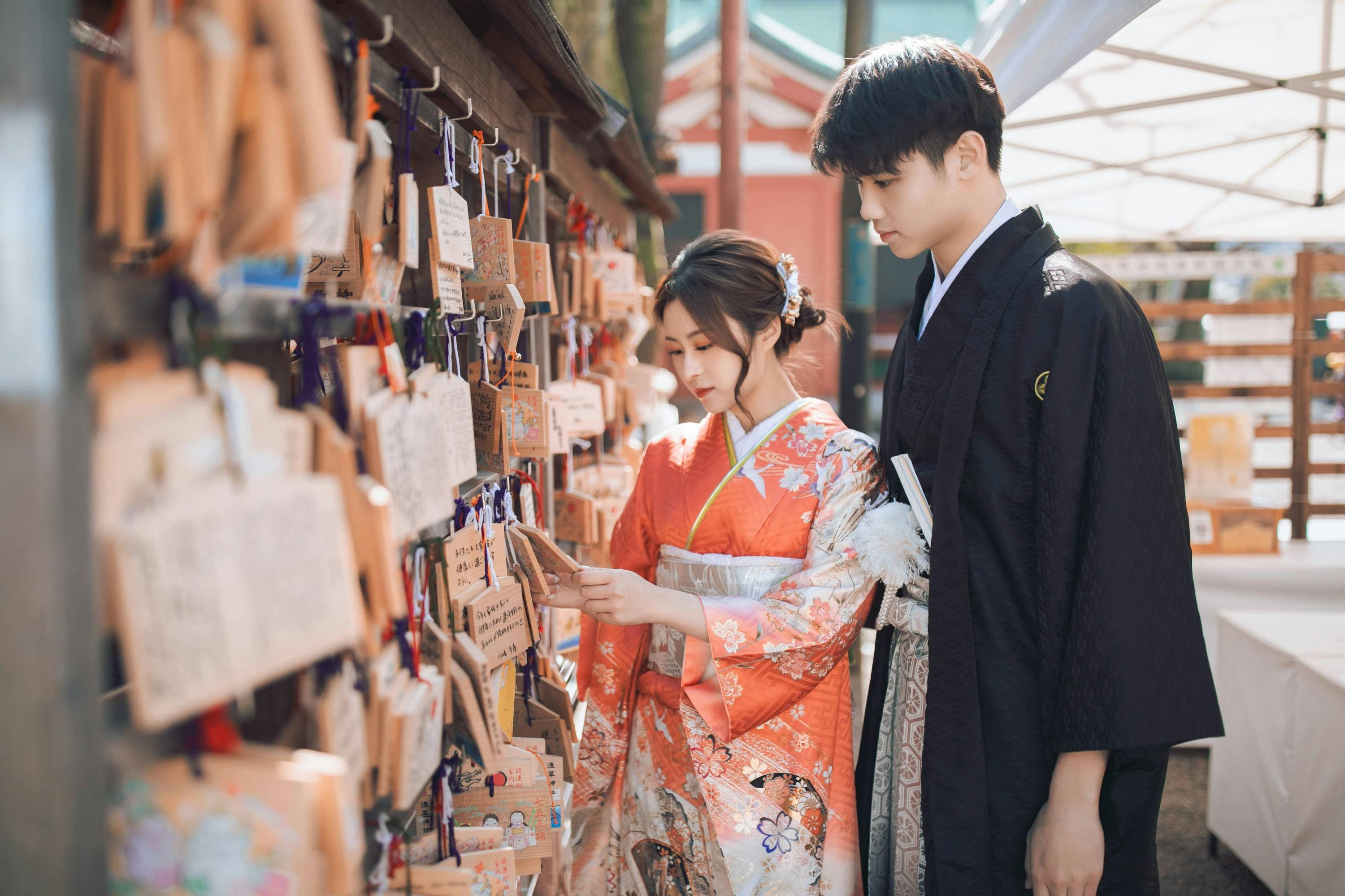 Two individuals in traditional attire reading wooden prayer plaques at a Shinto shrine.