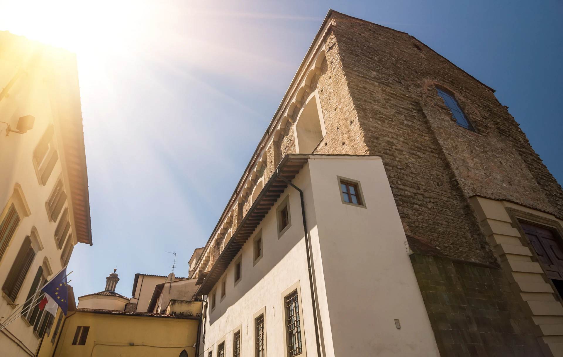 Sunlight shining over a historic stone and stucco building with arched windows under a clear blue sky.