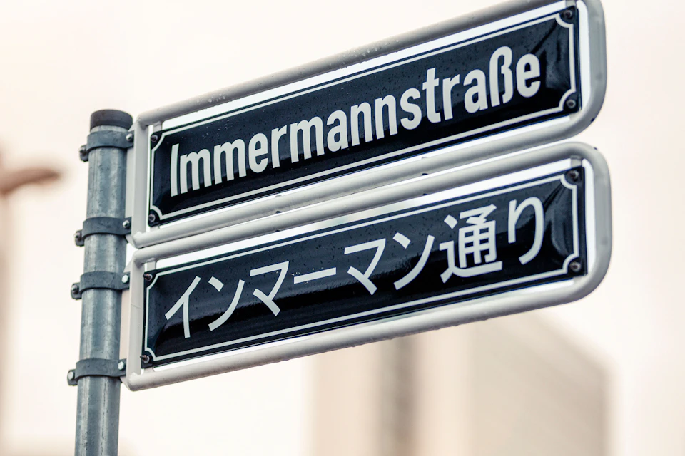 Two street signs in German and Japanese, both reading "Immermannstraße," mounted on a metal pole.