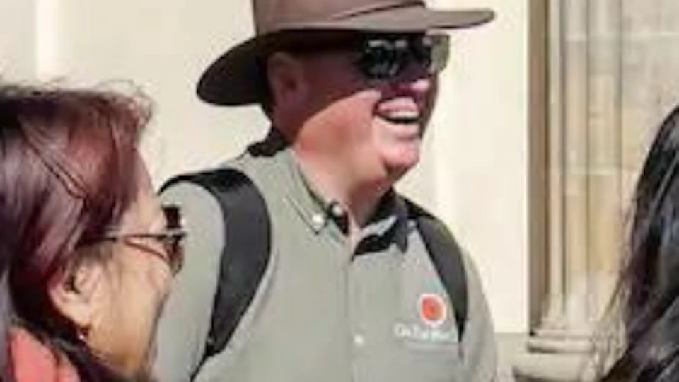 Tourist guide with a hat speaking to a group of people in front of large stone columns on a sunny day.