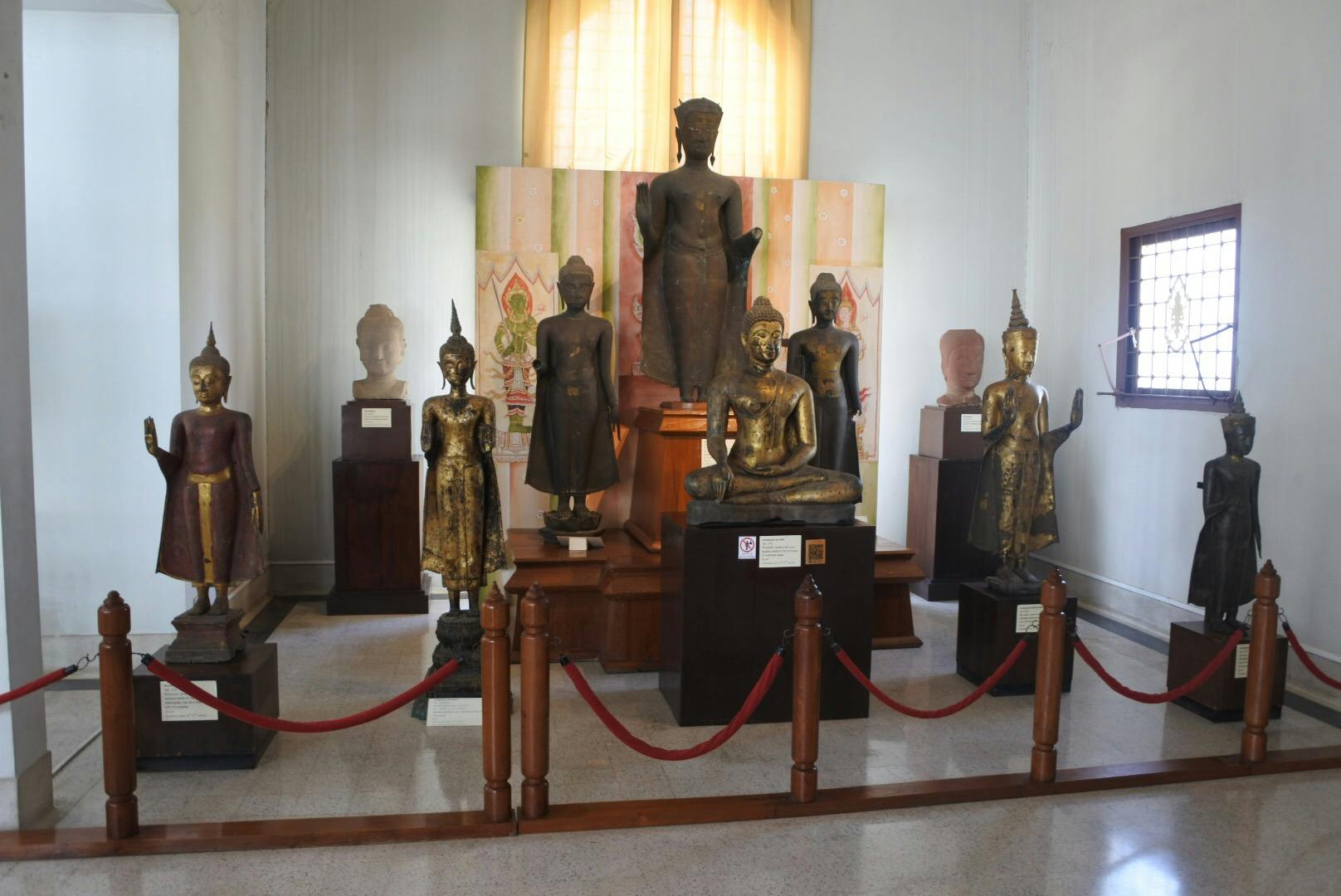 Salle où sont exposées diverses statues bouddhistes, notamment des sculptures debout, assises et des têtes, entourées de barrières en corde rouge.