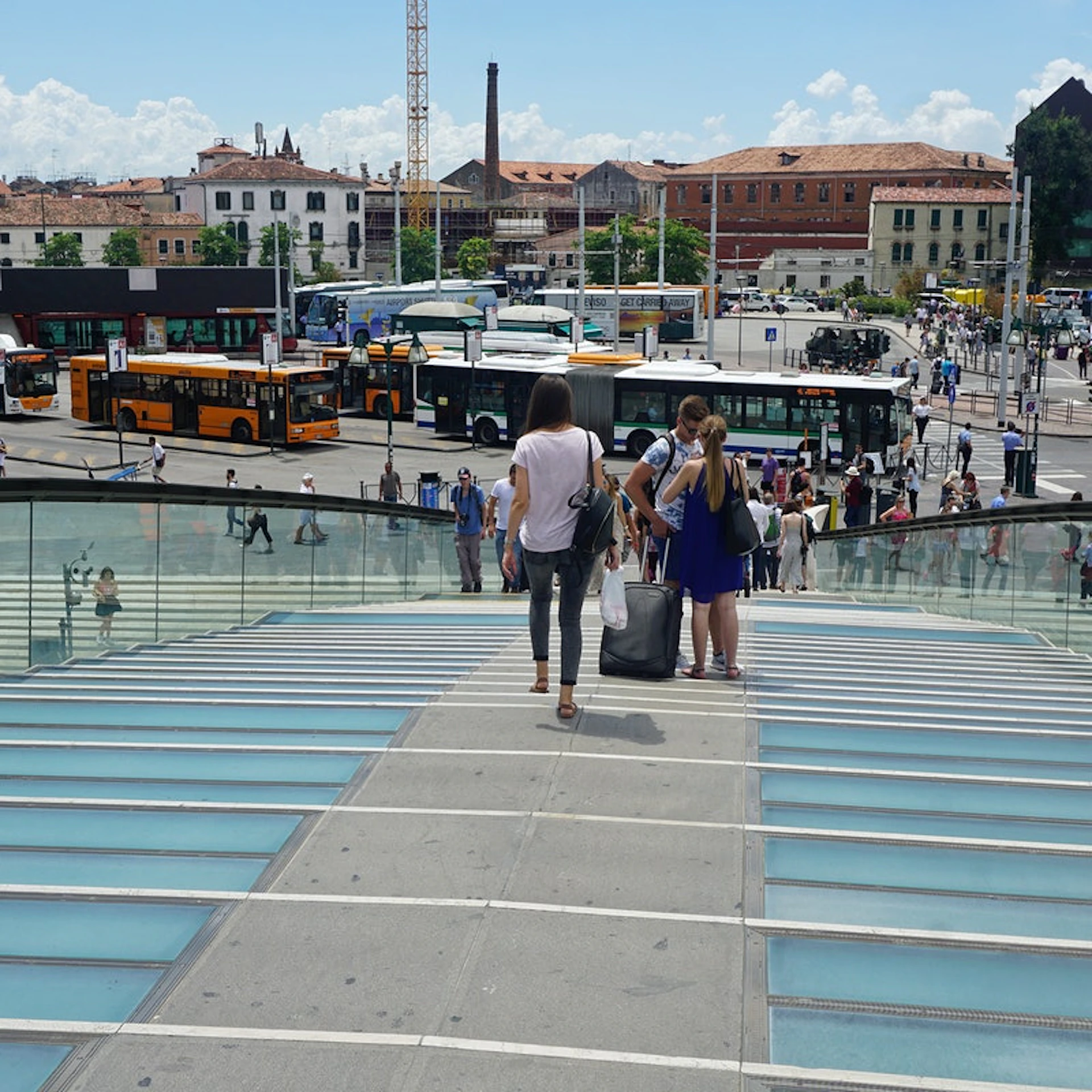 People walking down a glass and concrete staircase towards a busy street with buses and buildings in the background.